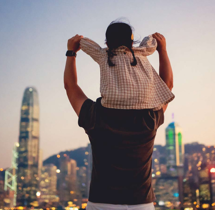 Child sitting on parent's shoulders with city skyline in the background