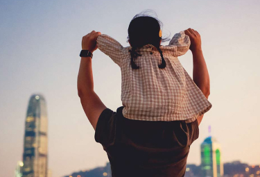 Child sitting on parent's shoulders with city skyline in the background