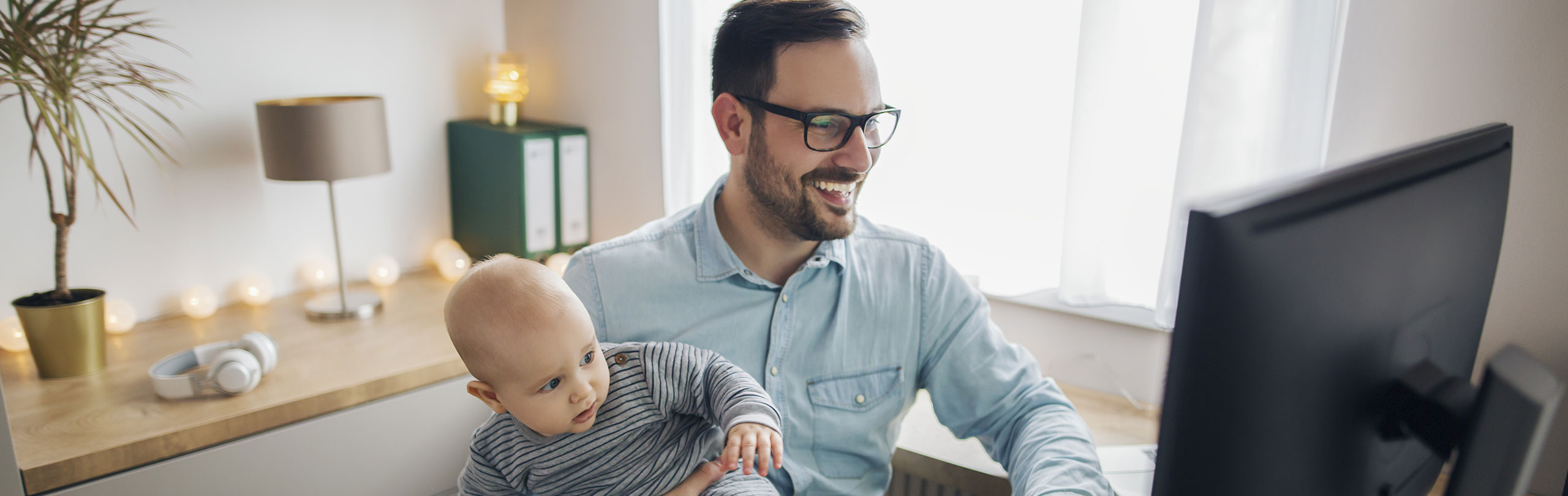 Man working at a computer holding a baby.