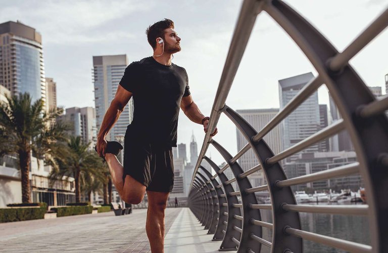 man in gym clothes stretching leg outside in city