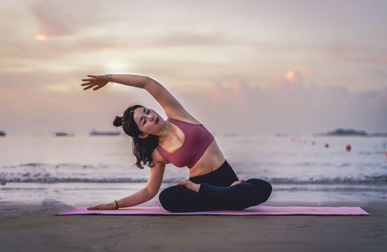 woman doing yoga stretch on the beach with the sea behind her