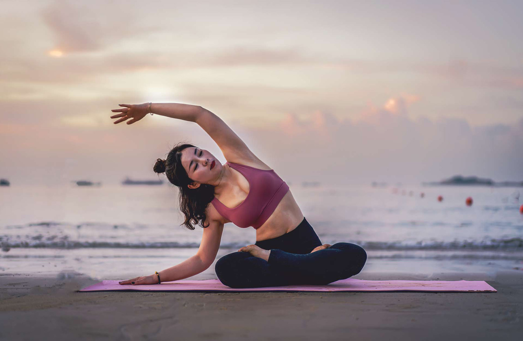 woman doing yoga stretch on the beach with the sea behind her