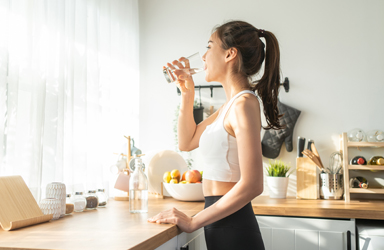 woman in gym clothes drinking water in a sunny kitchen