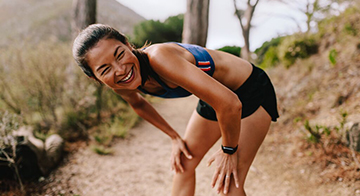 Woman running through uphill through woodland, stops to take a breath