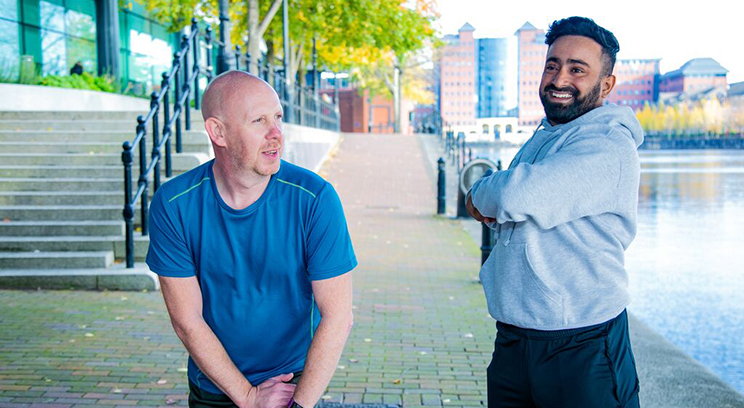 Two men stretch by the river during exercise