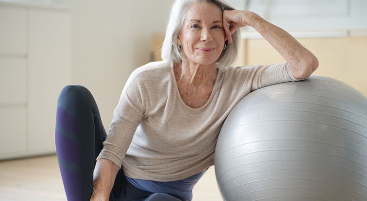 Woman in yoga wear sits on the gym floor, leaning on an exercise ball 