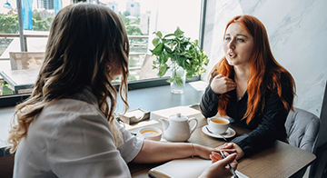 Two women talking in café touching hands. One has pen and notepad