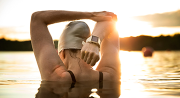 Woman in a lake wearing a swimming cap stretches 