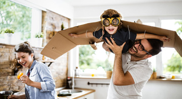 Father playing with their child who has cardboard wings and goggles on