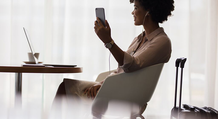 Businesswoman seated taking a mobile phone call, with open laptop and suitcase